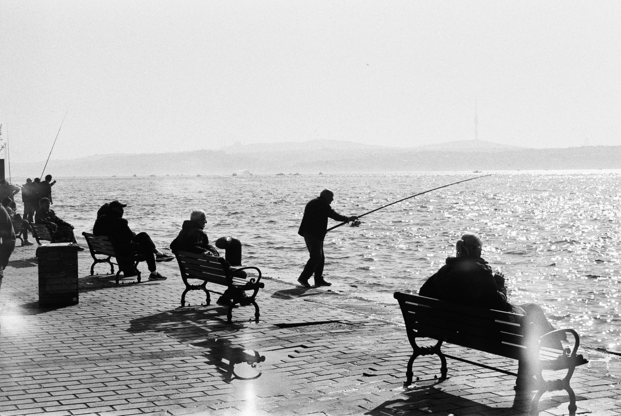Fishermen silhouetted on waterfront promenade